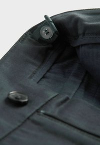 Musta kangasvuori, jossa on sileä tekstuuri, napilla suljettuna ja varmalla reunalla. Sisäpuoli on minimalistinen, ilman näkyviä kuvioita.