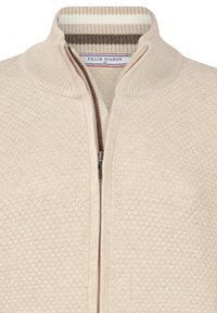 Gilet en tricot beige avec fermeture éclair sur le devant, col côtelé et motif texturé en nid d'abeille. L'intérieur présente une doublure rayée. Marque visible.