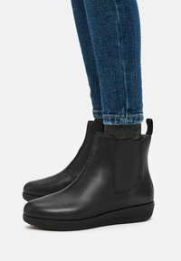 Schwarze Lederstiefeletten mit elastischen Seitenteilen und einer niedrigen Gummisohle, kombiniert mit dunkelblauen Jeans, die ein lässiges, schnittiges Design zeigen.