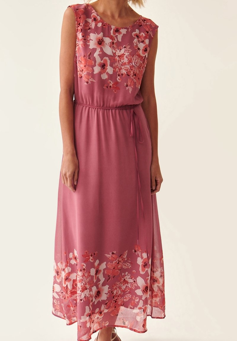 Robe maxi en tissu rose doux, ornée de motifs floraux dans des tons de corail et de blanc, avec une taille cintrée et une jupe fluide.