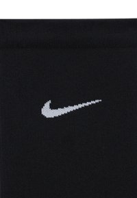 Svarte strikkede sokker med en hvit Nike Swoosh-logo på siden. Teksturen er jevn, med en ribbestrikket mansjett på toppen.