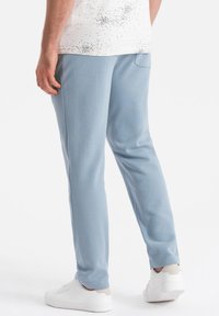 Helle blaue Jogginghosen aus weichem Stoff, mit schmaler Passform und Taschen an den Seiten, kombiniert mit weißen Sneakers auf einem hellen Hintergrund.
