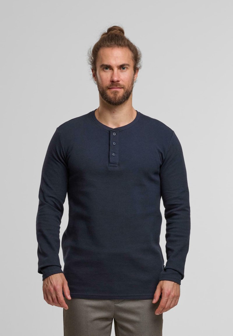 Felpa a maniche lunghe di colore blu navy realizzata in tessuto a costine, con patta a tre bottoni e scollo rotondo, abbinata a pantaloni con motivo. 