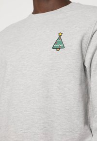 Felpa grigia con un piccolo albero di Natale verde ricamato e ornamenti rossi, con una stella gialla in cima. Tessuto morbido di cotone.