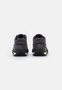 Des chaussures de sport gris foncé présentent un dessus en daim et en maille, un col rembourré et une semelle en caoutchouc noir avec des détails en blanc.