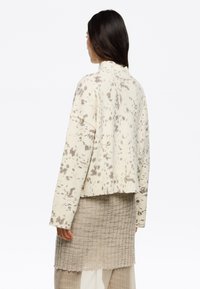 Maglione corto di colore crema con un motivo a trama texture e maculato e un colletto alto. Presenta maniche larghe e orlo a coste.