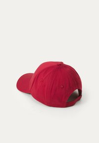 Red cotton baseball cap with a curved brim, adjustable back strap, and embroidered logo detail on the side. Smooth texture and fitted shape.