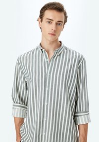 Camisa de botones a rayas con atrevidas rayas verticales en gris y blanco, mangas largas enrolladas hasta la mitad del antebrazo y una textura de tela suave.
