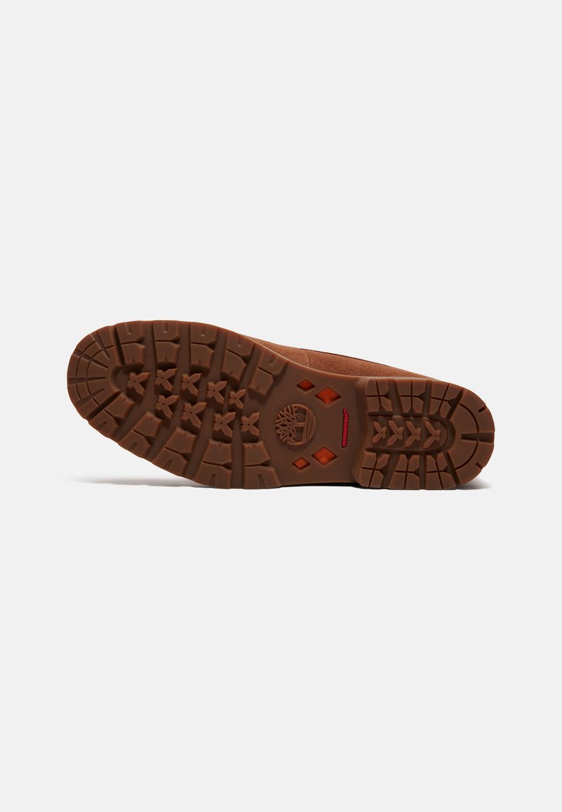 Suola in gomma marrone con motivo di grip testurizzato, caratterizzata da un logo e un accento rosso vicino al tallone. Mostra battistrada strutturato e stratificato per la trazione.