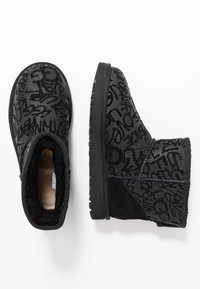 Botas negras hasta el tobillo hechas de ante, con un patrón texturizado de diseños similares a grafitis. Forro interior suave y suela de goma para mayor tracción.