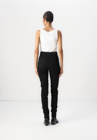 Blugi negri, mulati pe corp, cu talie inalta si doua buzunare la spate, asortați cu un top simplu alb. Textura netedă a materialului și designul minimalist.