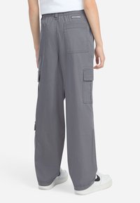 Person wearing gray wide-leg cargo pants with multiple pockets and white sneakers with black swoosh, shown from the back.