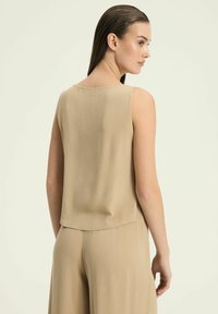 Beżowy bezrękawnik o teksturowanym wykończeniu, z zaokrąglonym dołem i luźnym krojem. Pokazany z tyłu, gładki, lekki materiał.