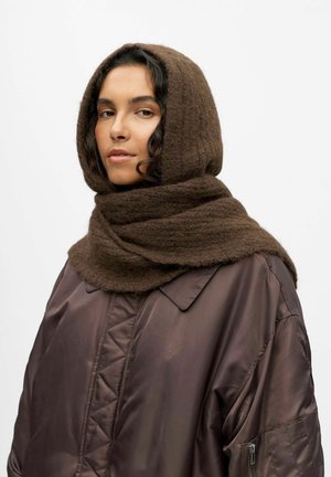 Écharpe en laine brune enveloppée autour de la tête et du cou, présentant une finition texturée. La personne porte une doudoune foncée et brillante avec un col.