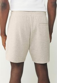 Vista trasera de una persona que lleva pantalones cortos beige claros con cinturilla elástica y un solo bolsillo trasero.