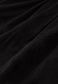 Černá semišová tkanina s hladkým povrchem, ukazující záhyby a detaily šití, zdůrazňující její měkký, hebký povrch.