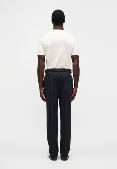 Φωτεινή μπεζ υφασμάτινη κοντομάνικη μπλούζα και σκούρο παντελόνι με σχέδιο, με σχεδιασμό ίσιου ποδιού. Μαύρα παπούτσια με γυαλιστερό φινίρισμα.