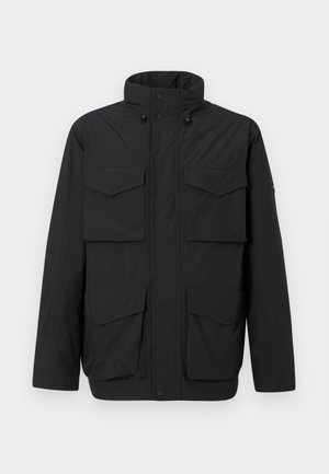 Svart isolert jakke med høy krage, frontglidelås, trykknapper og fire klaffelommer på en enkel lys bakgrunn.