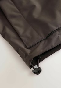 Manchon en tissu noir avec une couture cousue et un cordon de serrage réglable en bas, sur une surface claire.