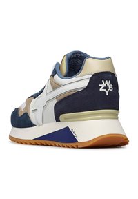 Sneaker z mieszanką niebieskiego, beżowego i białego zamszu oraz skóry. Posiada grubą białą podeszwę, podwyższony obcas oraz charakterystyczne logo z tyłu.