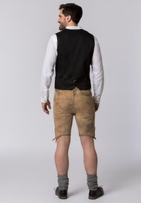Schwarze Herrenweste über einem weißen Hemd getragen, kombiniert mit braunen Lederhosen und grauen knielangen Socken, die einen klassischen Alpenstil präsentieren.