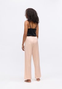 Zwarte satijnen cami met dunne bandjes, gecombineerd met lichtroze, luchtige broek met elastische taille, voorzien van een soepele textuur en wijde benen.