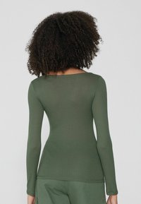 Langärmliges, ribbed Oberteil in Dunkelgrün, mit einem leicht scooped Ausschnitt und einer schmalen Silhouette. Weicher, dehnbarer Stoff.