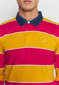 Långärmad polo-skjorta med breda horisontella ränder i rosa, gult och vitt, med en kontrasterande denimkrage och en knappslå.