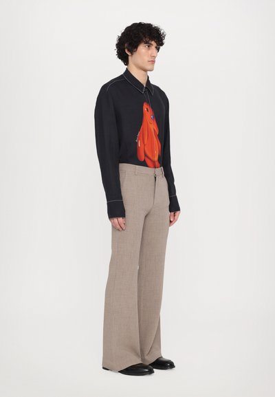 Long-sleeve black shirt with a red cartoon character design, paired with light brown wide-leg trousers and black footwear.