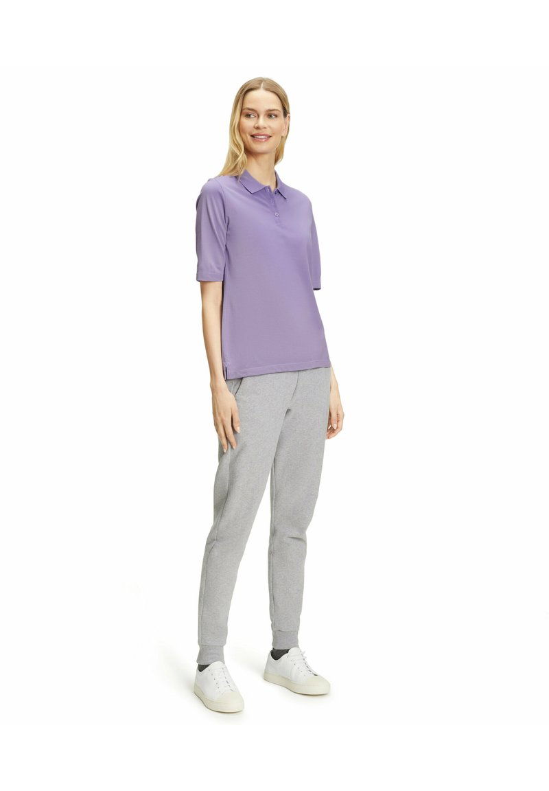 Kurzärmliges lila Polo-Shirt aus atmungsaktivem Stoff, kombiniert mit hellgrauen Jogginghosen und weißen Turnschuhen. Schlichtes und lässiges Design.