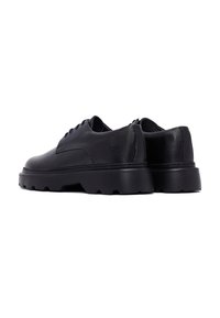 Chaussures en cuir noir avec un devant lisse, un dos texturé et une semelle en caoutchouc épaisse avec un motif robuste. Des lacets sont présents.