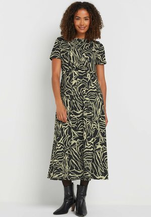 Schwarz-beige gemustertes Kleid mit kurzen Ärmeln, einer taillierten Taille und einem schwingenden Rock. Getragen mit schwarzen Ankle-Boots.