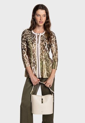 Oberteil mit Leopardenmuster, Reißverschluss vorne und Dreiviertelärmeln, kombiniert mit olivgrünen Hosen, dazu eine cremefarbene Bucket Bag haltend.