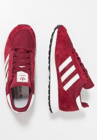 Röda sportiga sneakers i mocka och mesh-material, med tre vita ränder, en vadderad krage och en strukturerad svart gummisula.