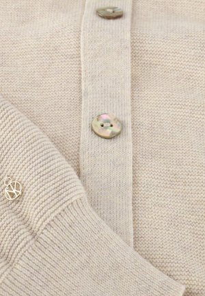 Beige gebreid vest met twee ronde parelachtige knopen dicht, met zichtbaar geribde manchetten en een gladde gebreide textuur.