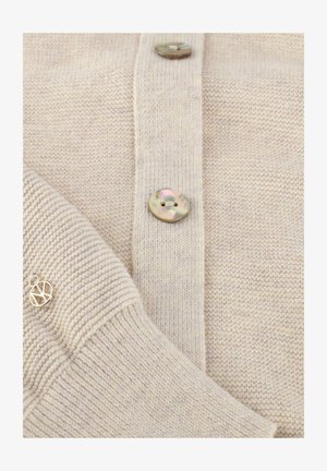 Beige gebreid vest met twee ronde parelachtige knopen dicht, met zichtbaar geribde manchetten en een gladde gebreide textuur.