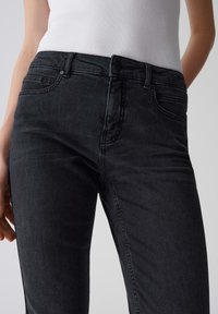 Jean en denim noir au design ajusté, doté de cinq poches, d'un devant à boutons et d'un dégradé subtil. Le matériau semble durable avec une texture lisse.