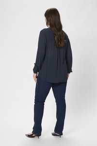 Mörkblå blus med lång ärm och avslappnad passform, plisserad bak, kombinerad med jeans i mörk tvätt och svarta pumps med spetsig tå.