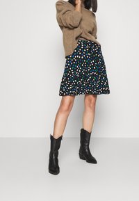 Tänkt stickad tröja, svart kjol med färgglada prickar, volangkant och svarta spetstövlar med spetsig tå. Texturerat material och lagerdesign.