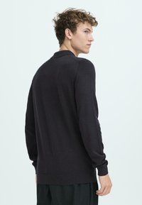 Mørk, let sweater med krave og lange ærmer. Har en glat tekstur og en lige pasform ved livet. Ingen synlige mønstre.