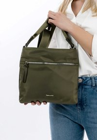 Olive green nylon handbag with a front zip pocket, dual handles, and a silver logo accent. Smooth texture and rectangular shape.