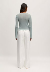 Helles blauer, gerippter Pullover mit langen Ärmeln und figurnaher Passform. Kombiniert mit weißen, weit geschnittenen Hosen, die einen lässigen Schnitt und eine glatte Textur aufweisen.