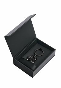 Black keychain with a circular ring and a shiny letter "B" design, placed in an open black box with a ribbon accent on the interior.