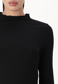 Black long-sleeve top with a textured fabric, featuring a slightly ruffled neckline and a fitted design.