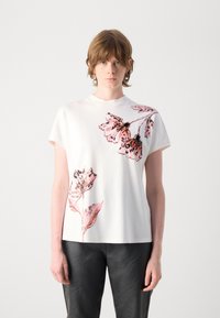 Witte T-shirt met korte mouwen, versierd met een roze bloemenprint aan de voorkant en een gladde textuur. Gepaard met zwarte leren broek.