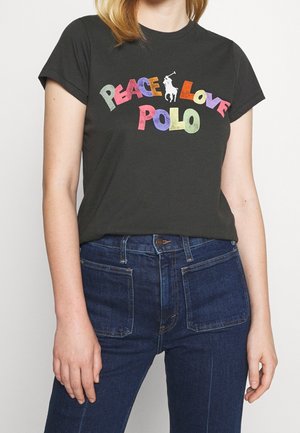 Kobieta nosząca czarny t-shirt z kolorowym napisem „Peace Love Polo” i logo gracza polo, połączony z wysokim stanem niebieskich dżinsów.