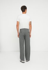 Graue, weit geschnittene Hose austexturiertem Stoff, ausgestattet mit einem normalen Bund und zwei Gesäßtaschen, kombiniert mit einem weißen T-Shirt.