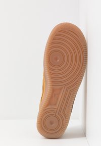 Semelle de chaussure avec un motif de relief ondulé et circulaire en caoutchouc marron clair, avec un logo Nike bien en vue près du bord.