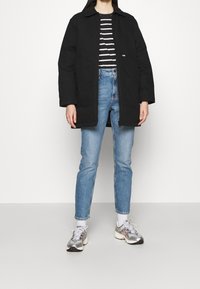 Sort frakke med krave, kombineret med en sort-hvid stribet skjorte og lyseblå jeans. Skoene er sølvfarvede med flerfarvede accenter.