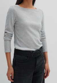 Ljust grå, långärmad tröja i mjukt stickat material, kombinerad med svart vävd bälte, bärs med mörka jeans.